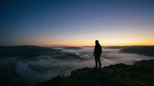 Silhouette contemplative dans un paysage de transition entre obscurité et lumière aube, symbolisant la traversée spirituelle